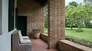 Uma área de estar coberta ao ar livre, com parede de tijolos, um banco e um vaso de planta.