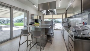 Eine moderne Küche mit Edelstahlgeräten, einer großen Kochinsel mit Barhocker und Blick auf eine angelegte Außenanlage.