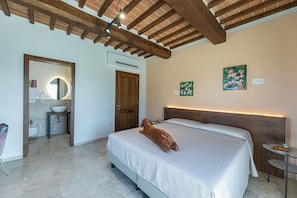 Ein Schlafzimmer mit Bett, Holzboden, Badezimmer mit Waschbecken und zwei Bildern an der Wand.