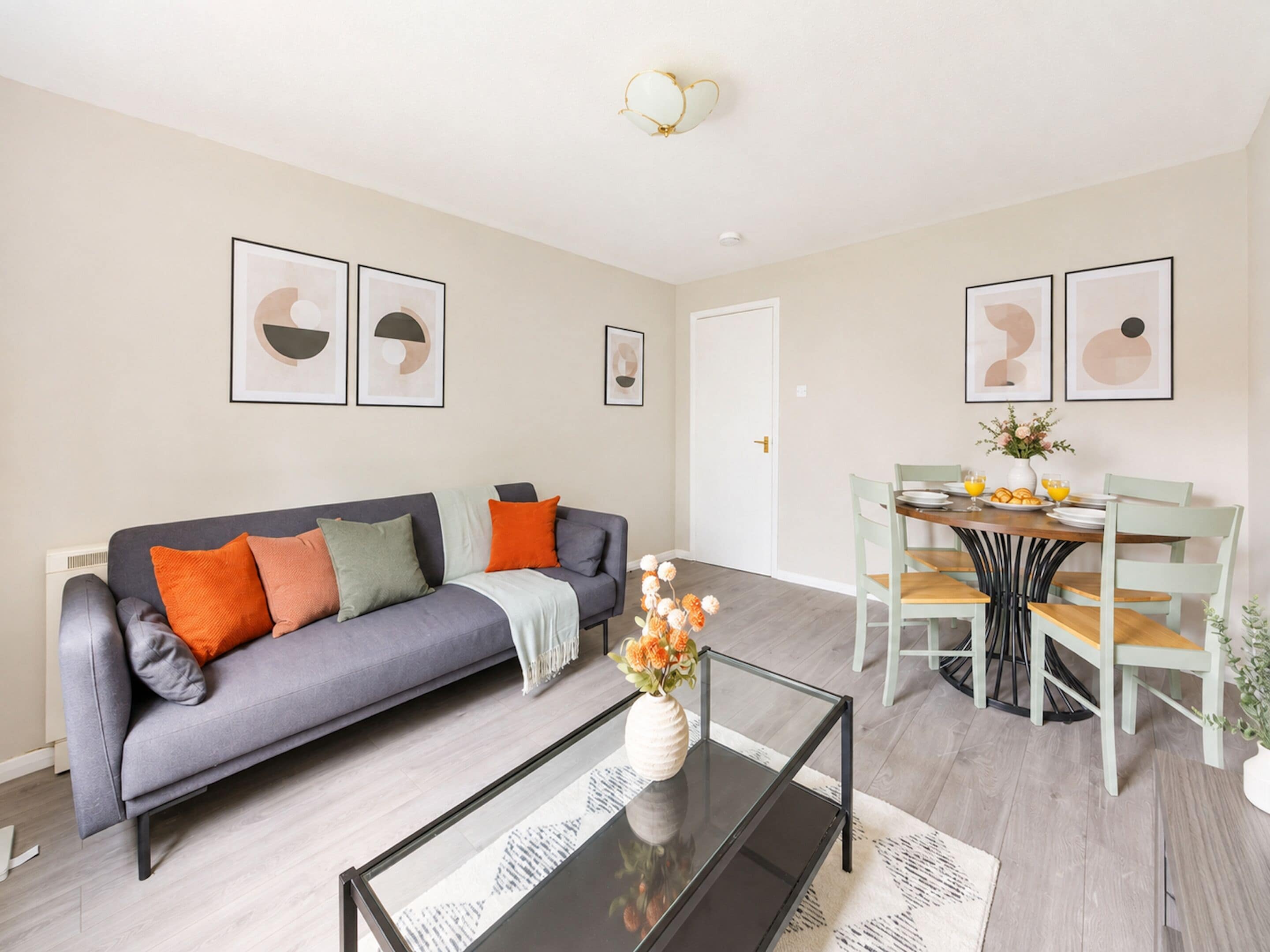 A modern living room with a grey sofa, a glass coffee table, and a dining area with a wooden table and chairs.