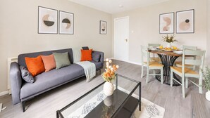 Una sala de estar moderna con un sofá gris, una mesa de centro de vidrio y un comedor con una mesa y sillas de madera.