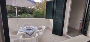 Ein Balkon mit Tisch und Stühlen, einer Schüssel mit Essen und einer teilweise geöffneten Tür.