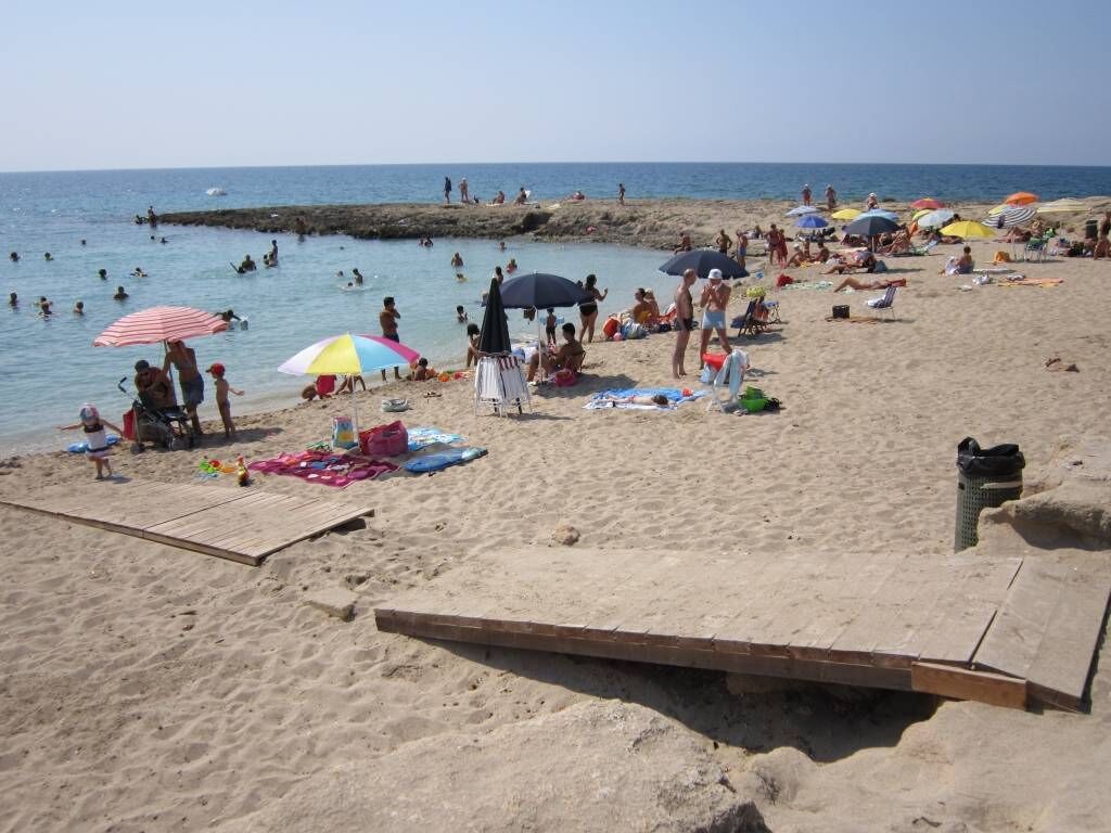 A beach with a wooden pier, umbrellas, and people relaxing on the sand.