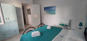 Een kamer met een bed, een bureau, een stoel, een kledingkast en een schilderij aan de muur.
