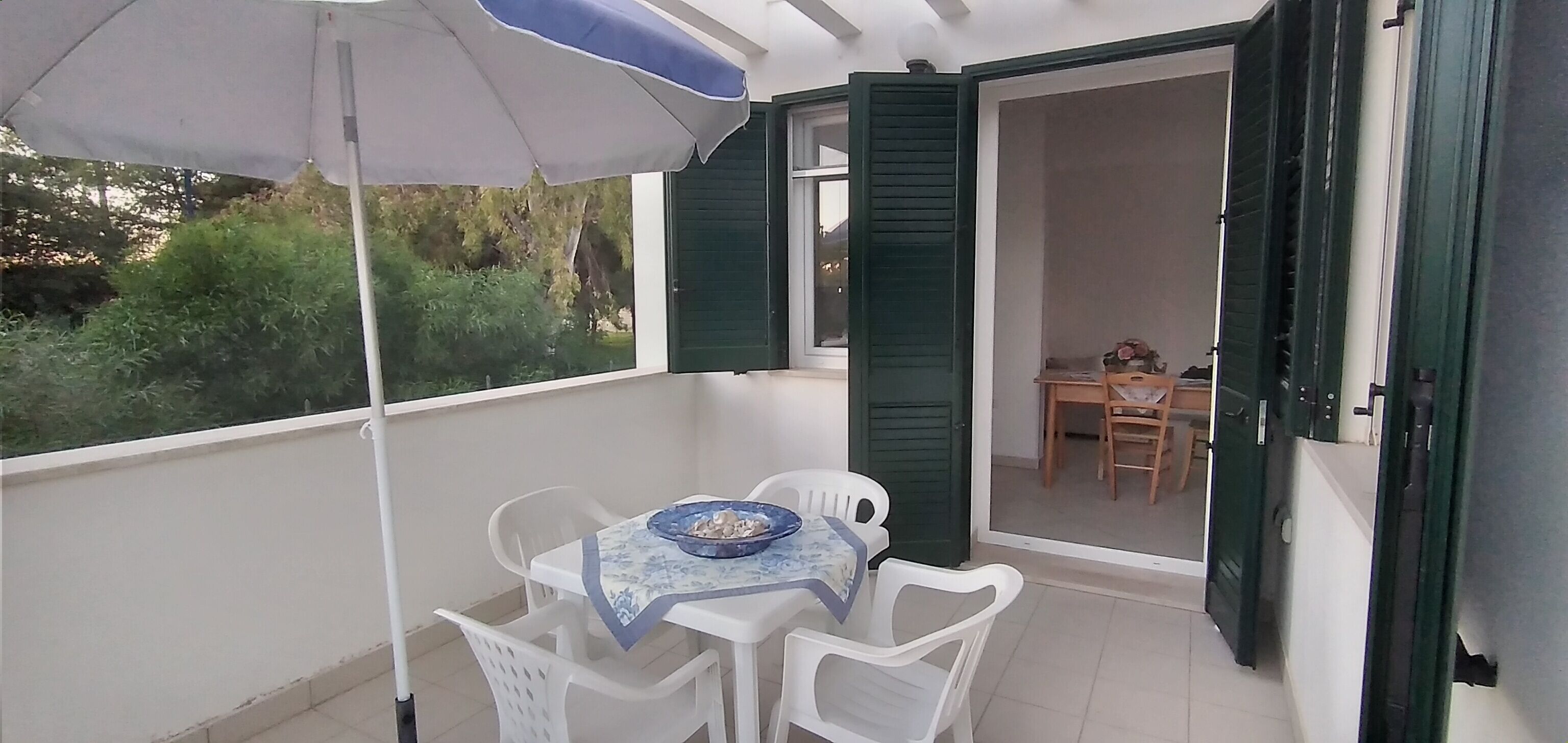 Un balcón con una mesa, sillas y una sombrilla, con vistas al jardín.