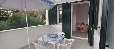 A balcony with a table and chairs, an umbrella, and a view of the garden.