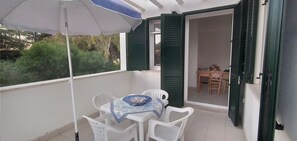 Een balkon met een tafel, stoelen en een parasol, met uitzicht op de tuin.
