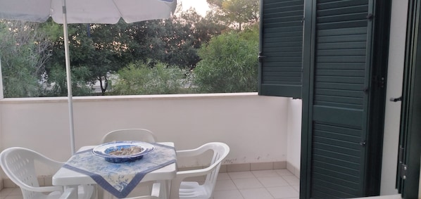 Ein Balkon mit Tisch und Stühlen, einer Schale und einer teilweise geöffneten grünen Tür.