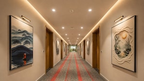 A hotel hallway with a carpeted floor, wooden doors, and framed artwork on the walls.