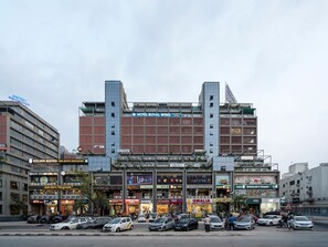 A multi-story hotel with a prominent sign for 'HOTEL ROYAL WING' and various commercial establishments on the ground floor.