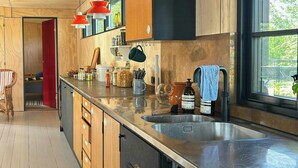 A modern kitchen with wooden cabinets, a stainless steel countertop, and a large window providing natural light. - Beach house with sea view in Røsnæs (Kalundborg)