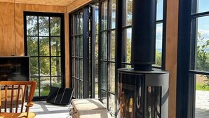 A cozy room with a large window, a black wood-burning stove, a wooden chair, and a small table. - Beach house with sea view in Røsnæs (Kalundborg)
