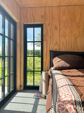 Ein Zimmer mit einem Bett, einem Fenster und einer zur Außenwelt führenden Tür.