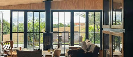 A spacious room with large windows, wooden flooring, and a cozy seating area with a fireplace.