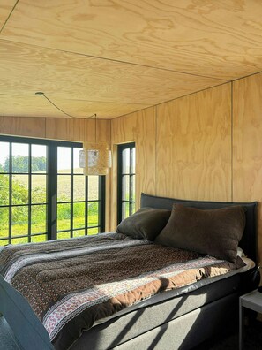 A bedroom with a large window, a bed with patterned bedding, and a woven light fixture. - Beach house with sea view in Røsnæs (Kalundborg)