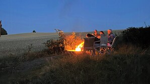 A campfire with two people sitting on chairs, surrounded by grass and a field. - Beach house with sea view in Røsnæs (Kalundborg)