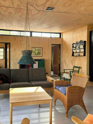 A room with a wooden ceiling, a hanging light fixture, a sofa, a wicker chair, a table, and a wall-mounted plate rack. - Beach house with sea view in Røsnæs (Kalundborg)