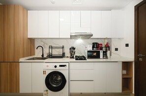 A compact kitchen with white cabinets, a built-in washing machine, a coffee maker, and a microwave. - Bloomfields Studio in Elysee 3 (Dubai)