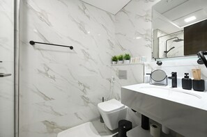 A modern bathroom with a white marble wall, a glass shower enclosure, a white sink with black fixtures, and a toilet. - Bloomfields Studio in Elysee 3 by Pantheon (Dubai)
