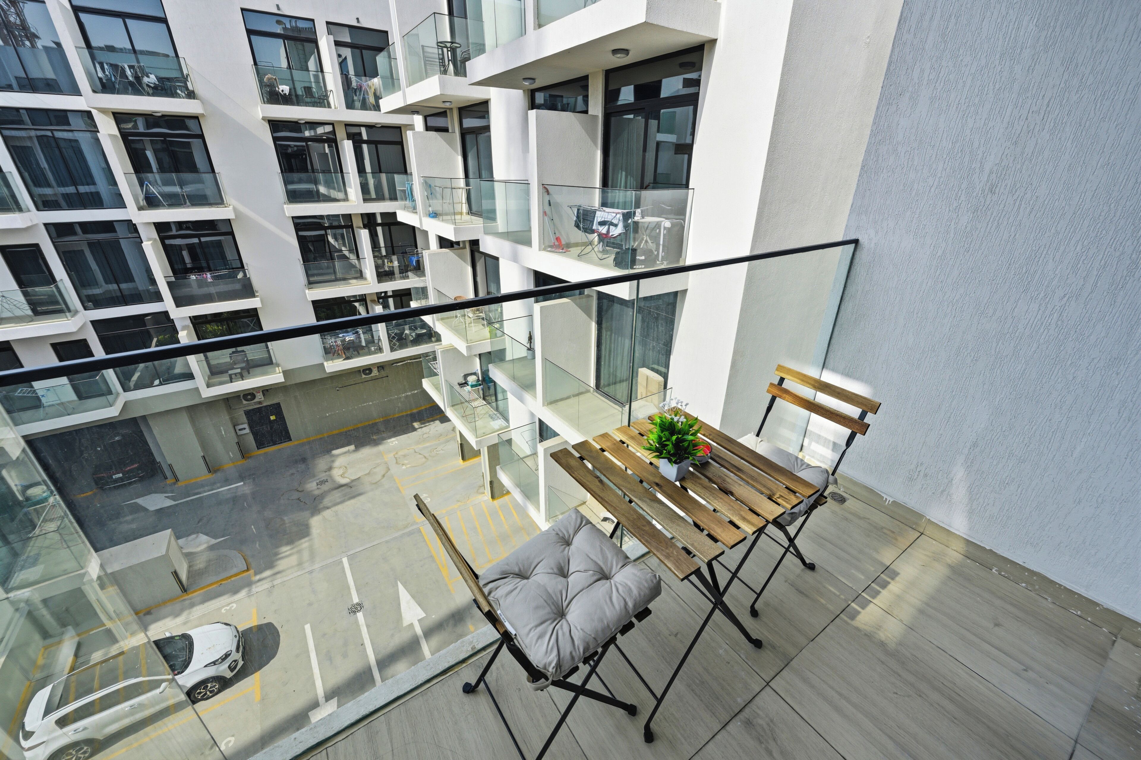 A high-rise building with a glass balcony, a wooden table, a bench, and a potted plant.