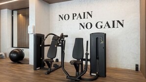 Ein Fitnessstudio mit Trainingsgeräten und einer Wand, auf der 'NO PAIN NO GAIN' steht.