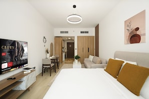 Quarto de hotel moderno com uma cama, televisão, área de refeições e cozinha.
