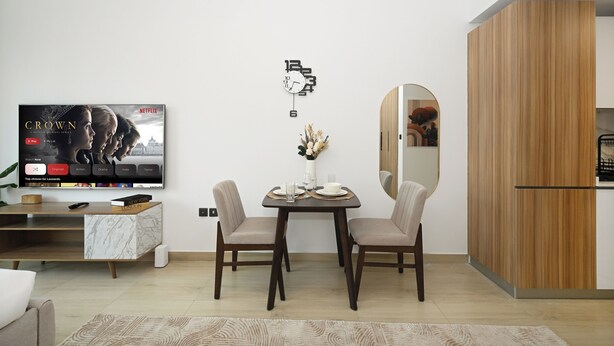 Ein modernes Wohnzimmer mit Esstisch, Stühlen, Fernseher und einer Holzkommode.