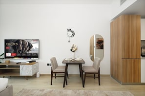 A modern living room with a dining table, chairs, a TV, and a wooden cabinet. - Bloomfields Studio in Elysee 3 by Pantheon (Dubai)