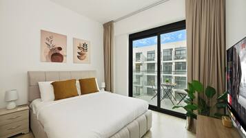 Habitación de hotel moderna con una cama grande, televisión y balcón con vista a la ciudad.
