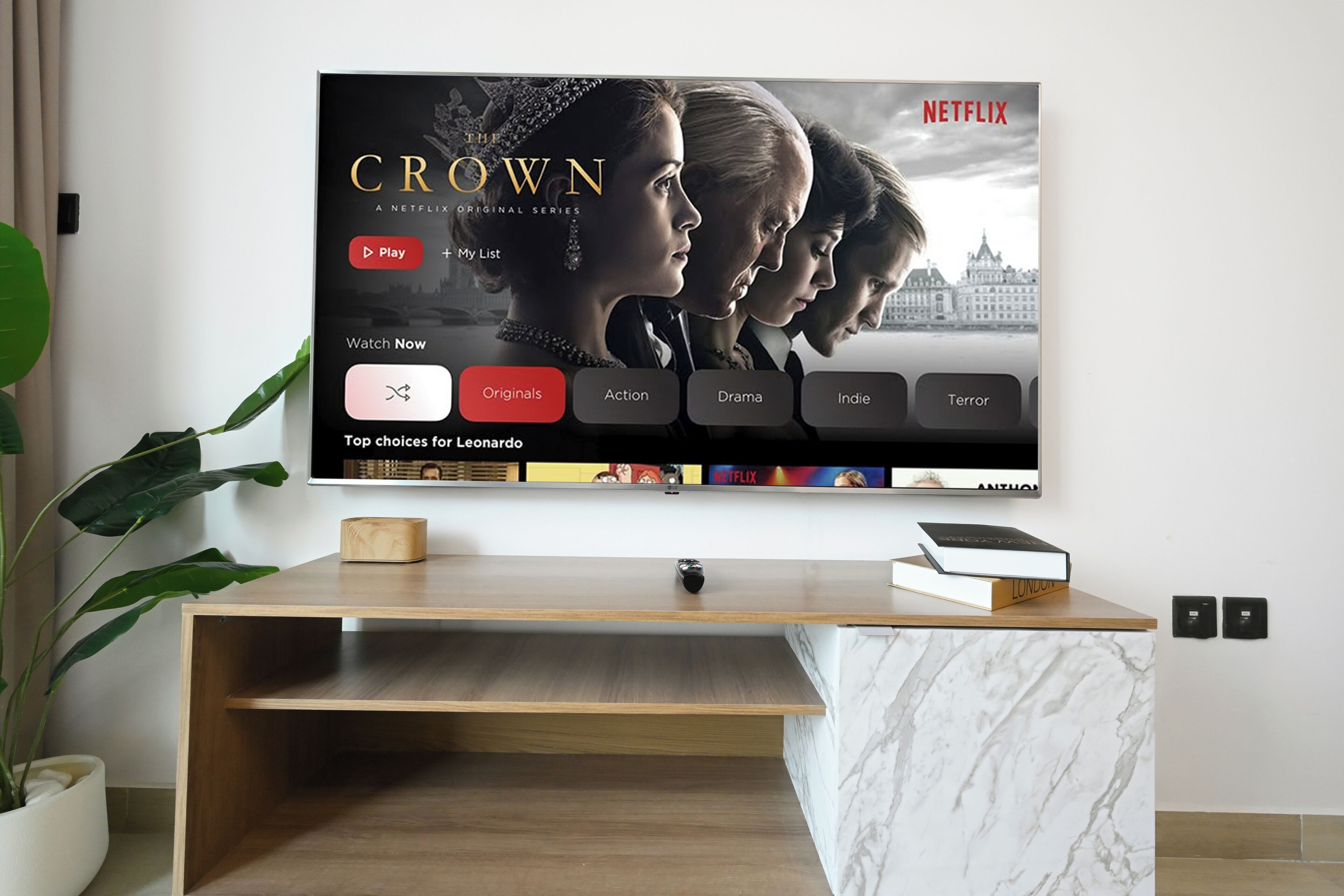 Televisor de pantalla plana montado en la pared mostrando una serie de Netflix titulada 'CROWN'.