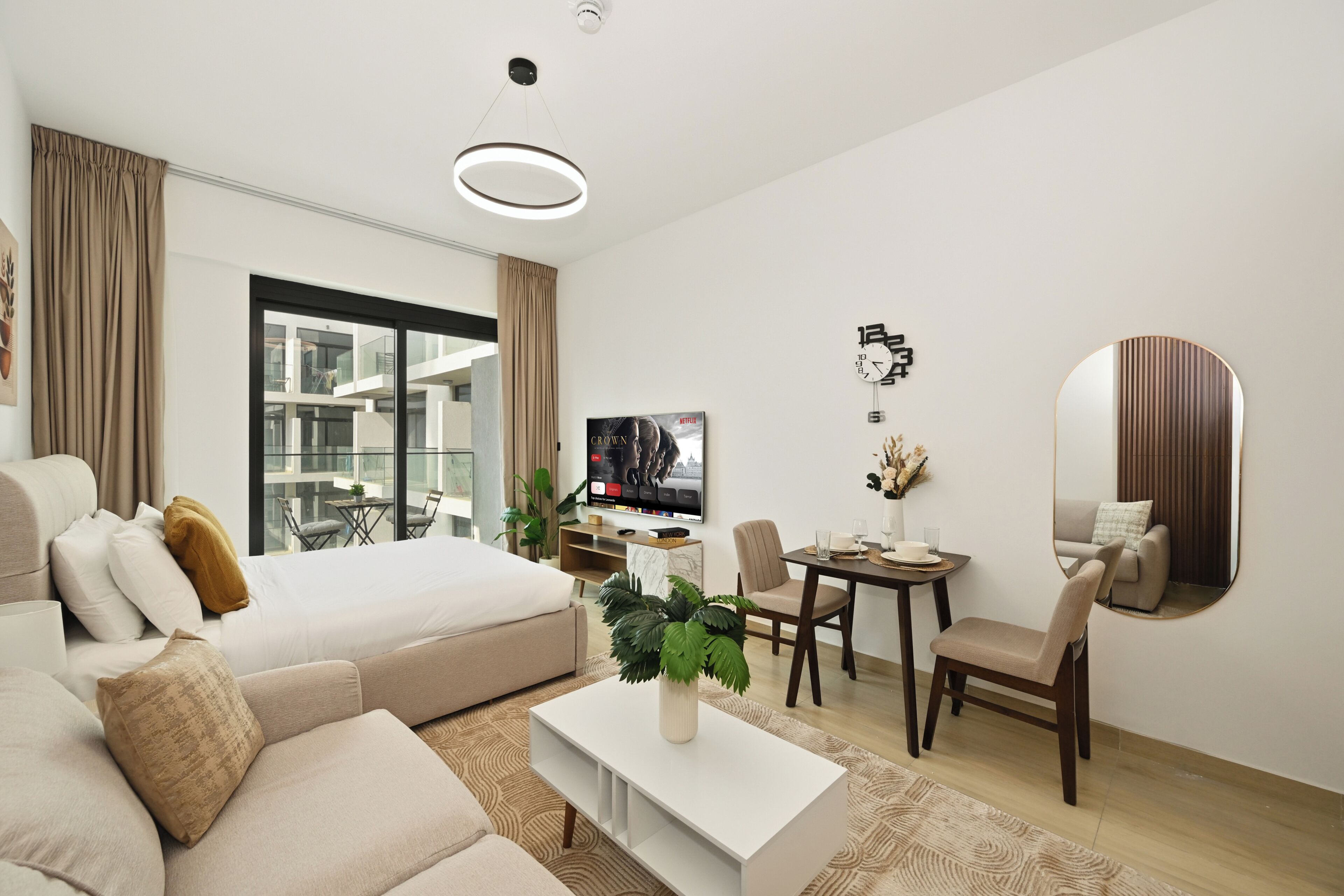 A modern hotel room with a bed, sofa, dining table, and a TV.