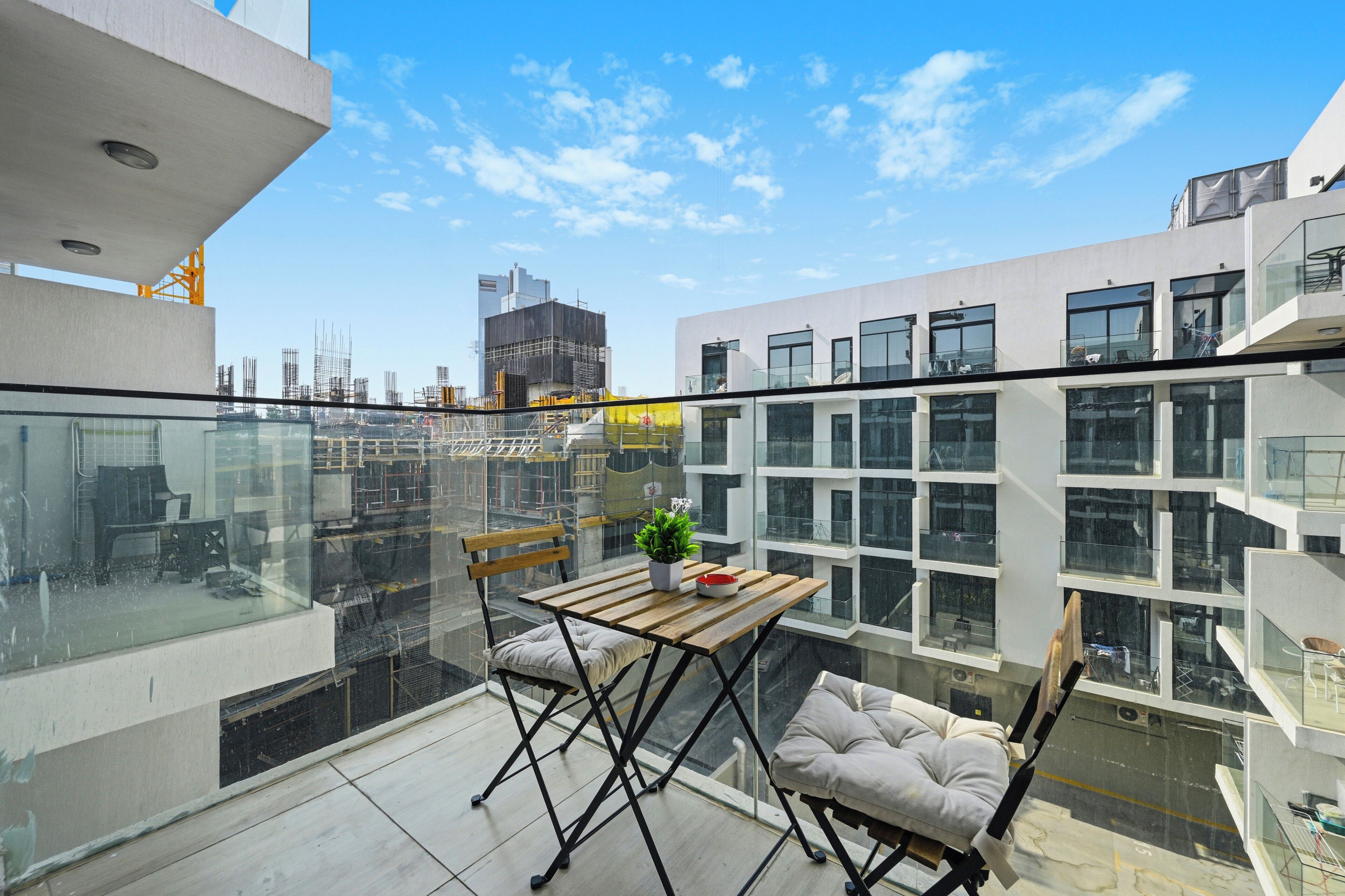 A balcony with a wooden table and chairs, a potted plant, and a view of the cityscape.