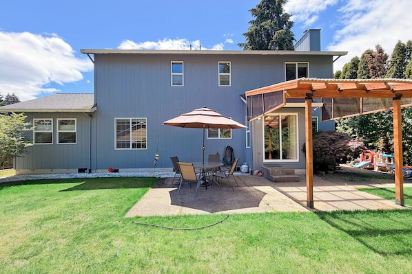 Une maison dotée d’un patio comprenant une table et des chaises, un parasol et une pergola en bois.