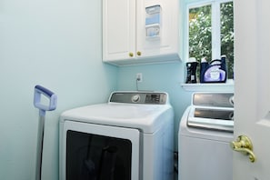 A laundry room with a front-loading washer and dryer, a wall-mounted drying rack, and a window with a view of greenery. - Peaceful 5-Bed Home at Road's End by Woods & Berry Farm, near Parks & Intel/Nike (Hillsboro)