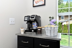 A coffee machine on a counter with a coffee cup, a basket of coffee pods, and a window with a view of trees and a house. - Peaceful 5-Bed Home at Road's End by Woods & Berry Farm, near Parks & Intel/Nike (Hillsboro)