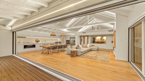 Uma sala de estar espaçosa com piso de madeira, uma área de jantar com mesa de madeira, e uma cozinha ao fundo.