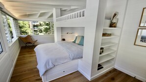 Quarto com beliche, uma cadeira, mesa de cabeceira e prateleira com livros e um objeto decorativo.