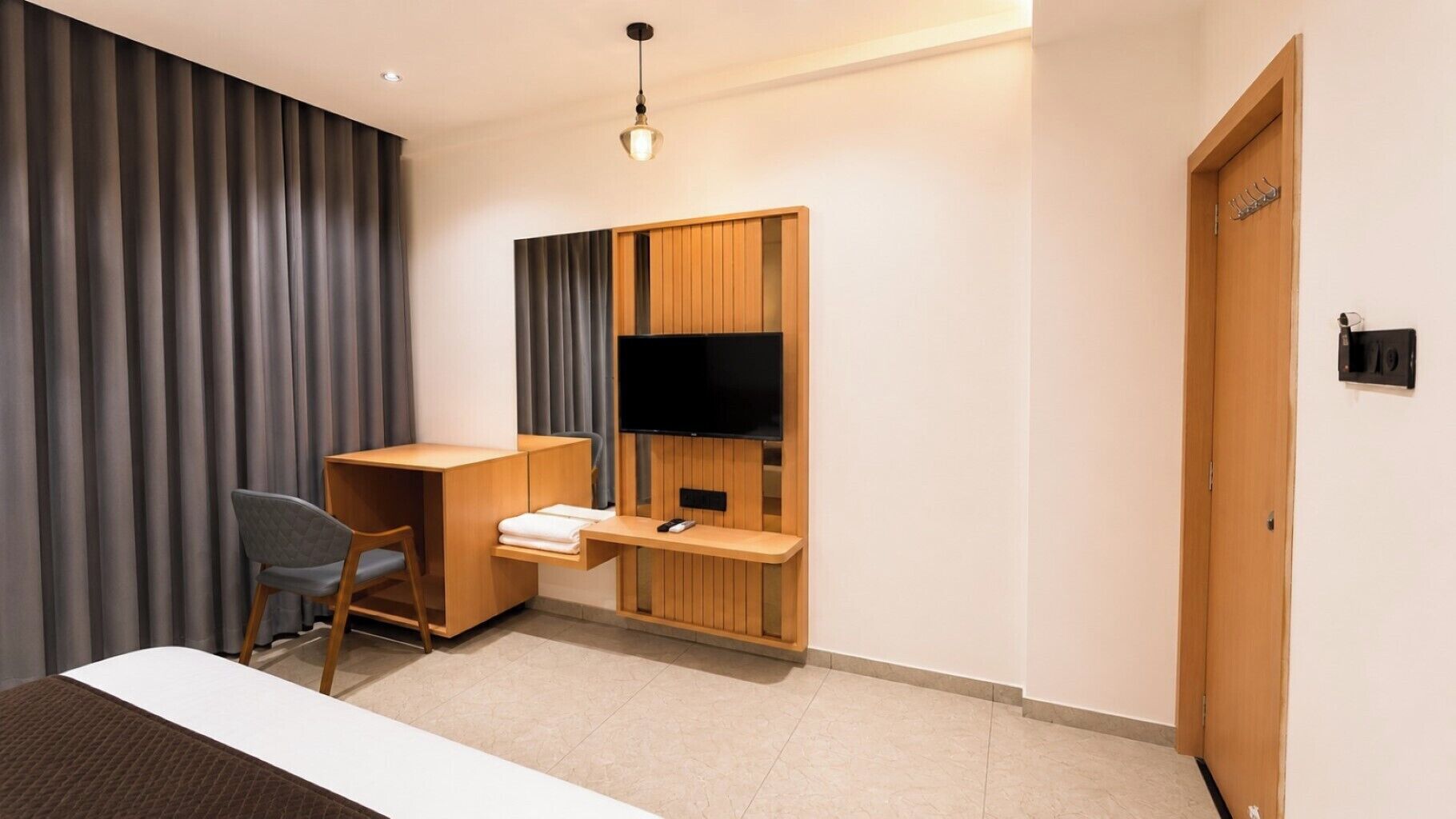 Habitación de hotel con cama, escritorio con silla, televisor fijado a un panel de madera y una puerta con perchero.