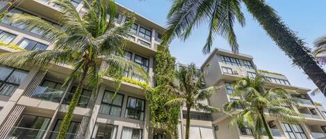 A multi-story hotel with balconies, large windows, and palm trees.