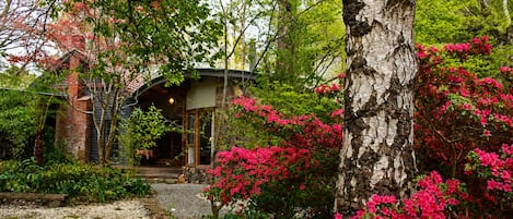 Una casa rustica con facciata in pietra, immersa nel verde e circondata da vivaci fiori rosa.