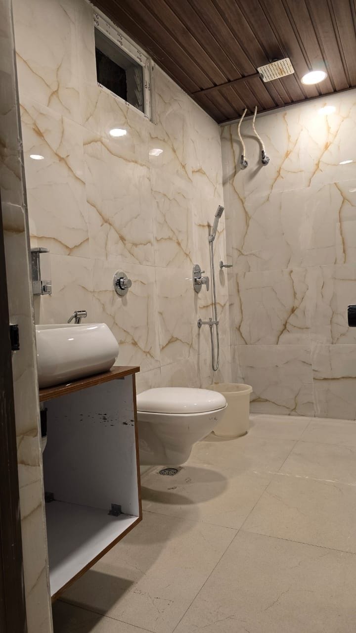 A bathroom with a marble wall, a toilet, a sink, and a shower area.
