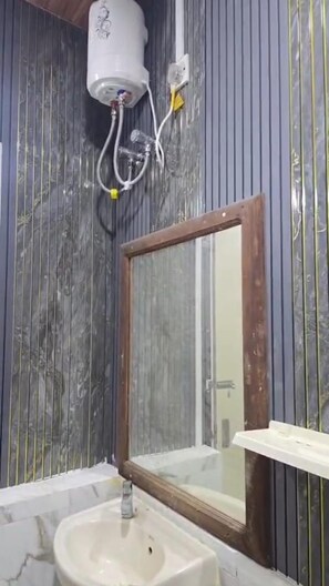 Ein Badezimmer mit Marmorwaschbecken, einem Spiegel und einem weißen Warmwasserbereiter an der Wand.
