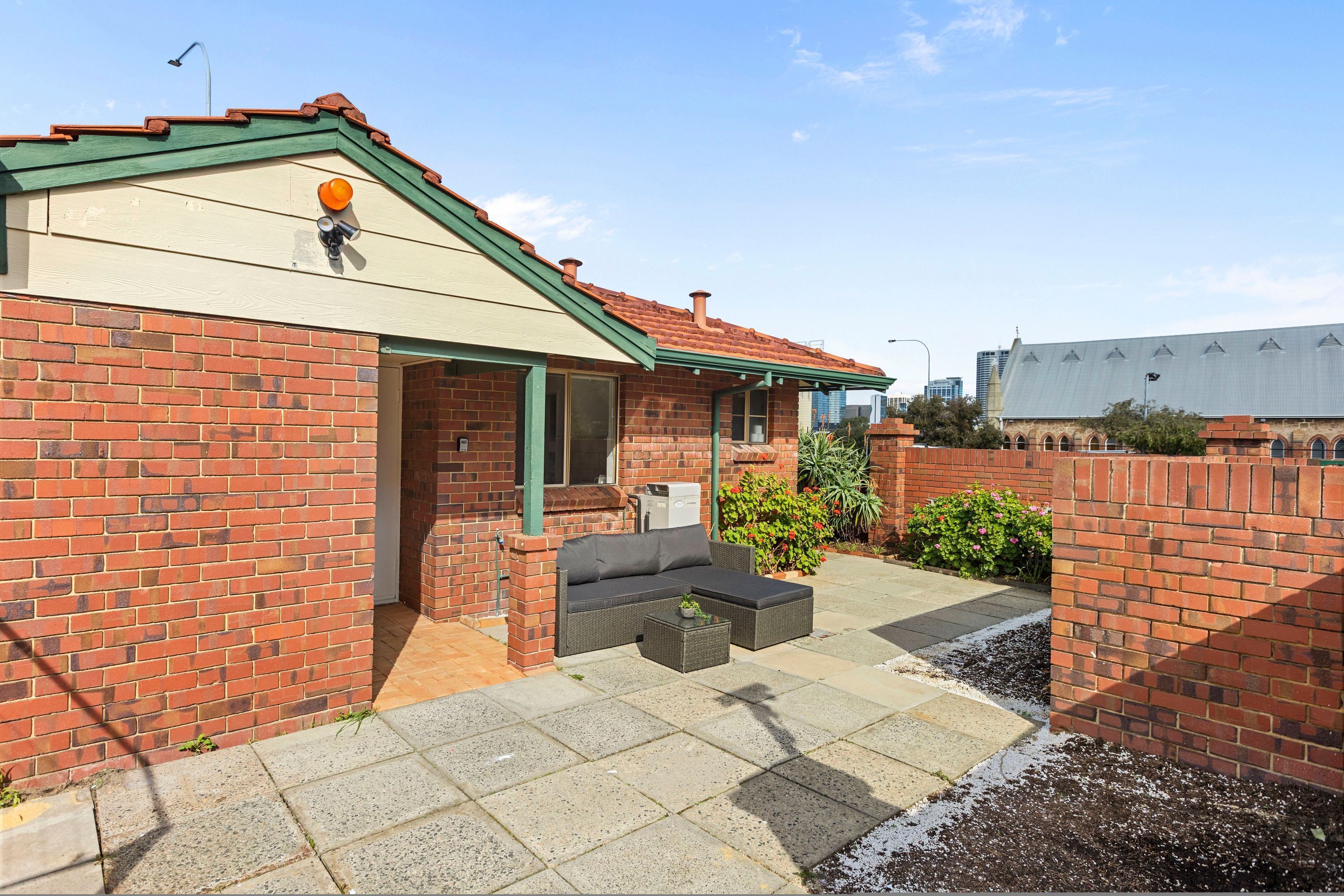 A brick house with a green roof, a patio with outdoor furniture, and a garden area.