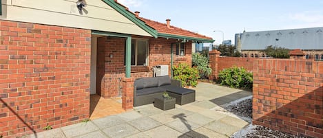 A brick house with a green roof, a patio with outdoor furniture, and a garden area.