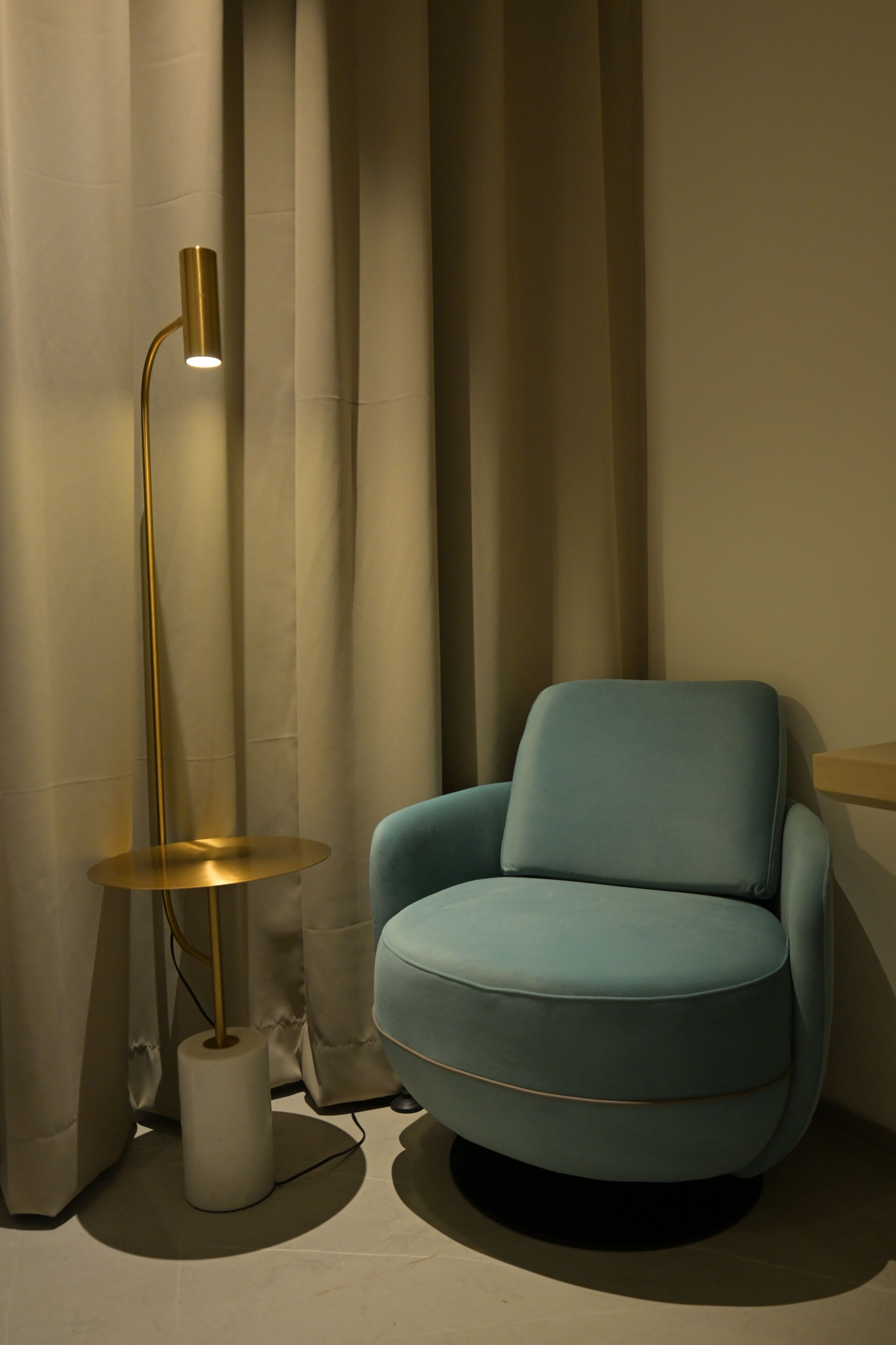 A room with a blue armchair, a floor lamp, and a curtain.