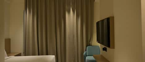 A hotel room with a bed, a chair, a TV mounted on the wall, and a ceiling fan.