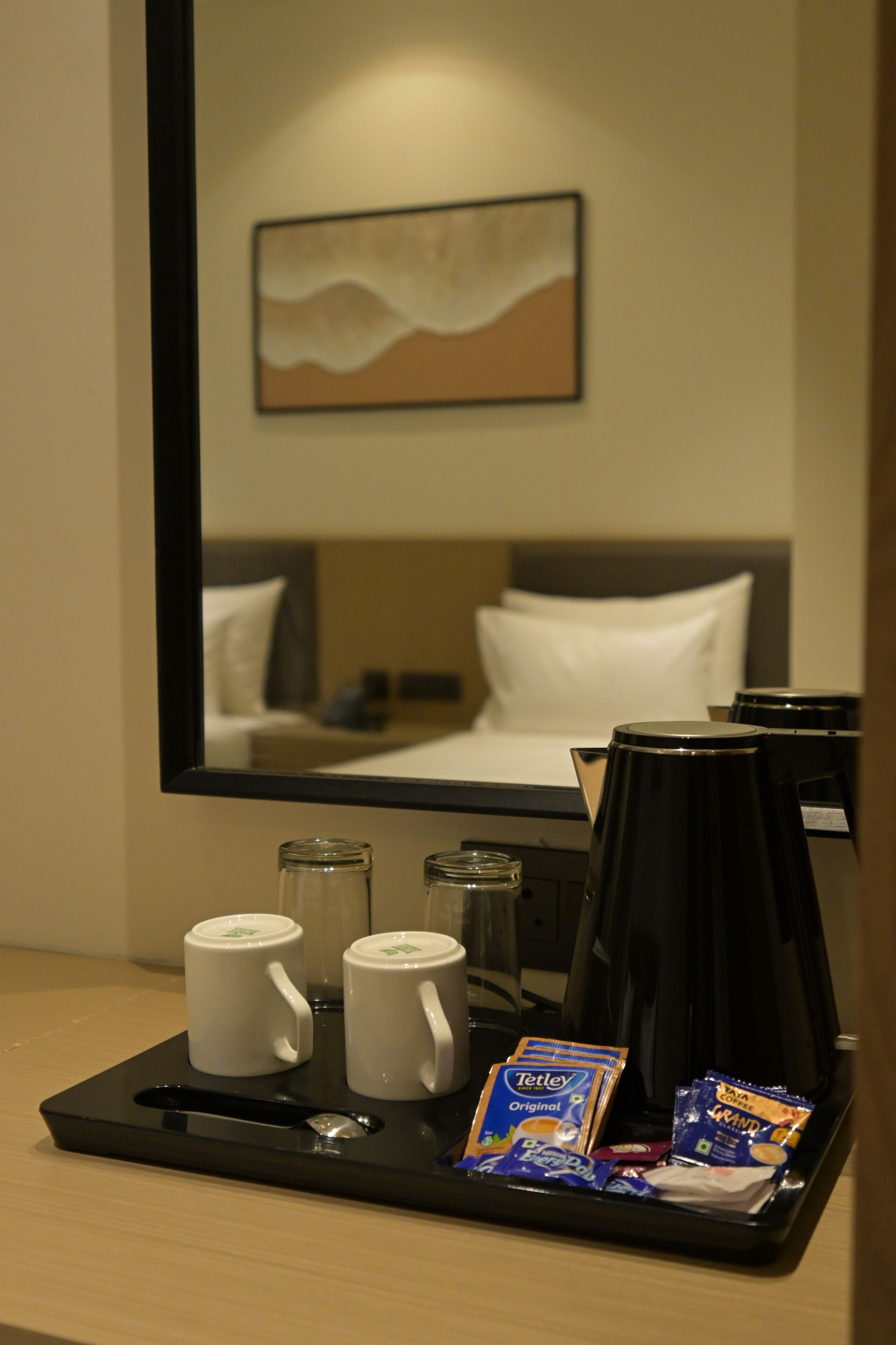 A hotel room with a bed, a coffee maker, two mugs, and a tray with coffee packets.