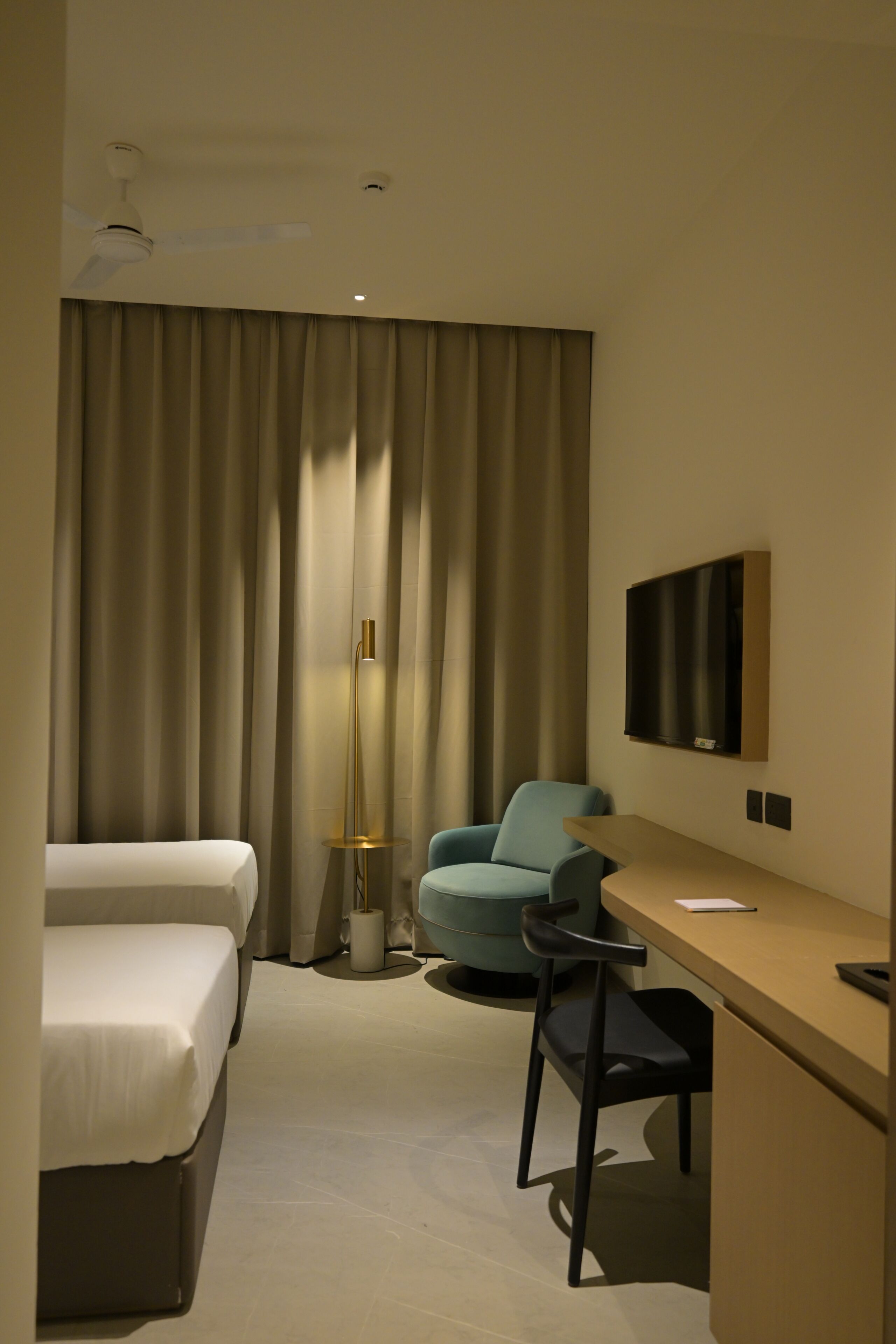 Une chambre d’hôtel avec un lit, un bureau, une chaise, une télévision et un rideau.