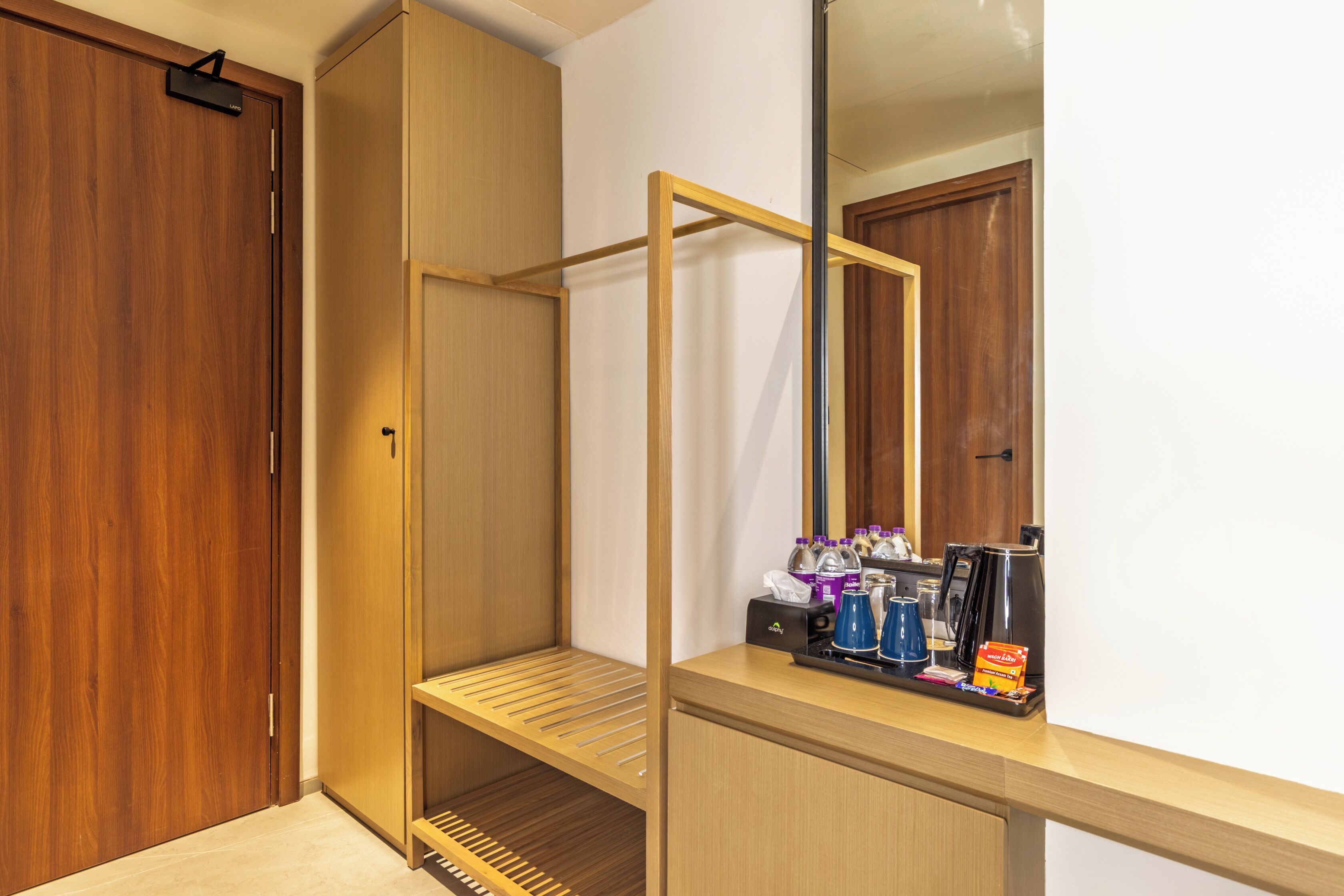 Quarto de hotel com guarda-roupa de madeira, espelho e uma pequena mesa com cafeteira e sachês de chá.