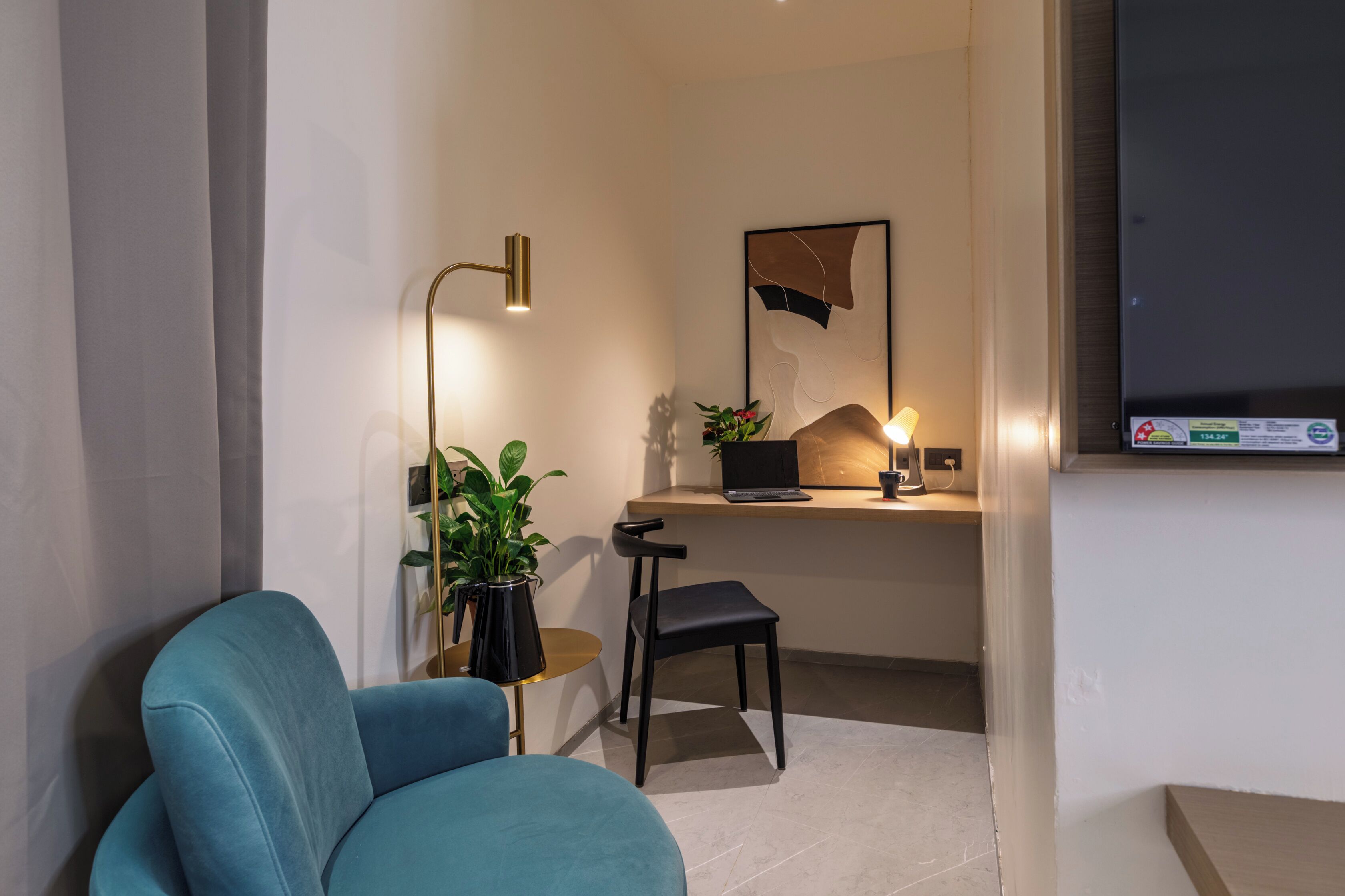 Quarto moderno com uma poltrona azul, uma escrivaninha com um laptop, uma planta e um abajur.